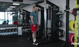 Mężczyzna wykonuje ćwiczenia na biceps przy użyciu wyciągu. W tle widoczne są sztangi, hantle i talerze obciążeniowe.