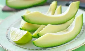 Plasterki awokado i ćwiartka limonki na talerzu. Zdrowe tłuszcze i niskie avocado kalorie.