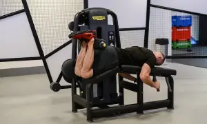 Mężczyzna wykonuje ćwiczenie na maszynie do uginania nóg leżąc (hamstring curl), budując siłę tylnej części uda.
