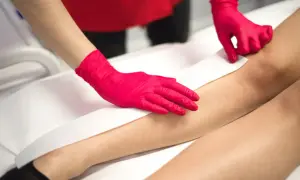 Depilacja woskiem w domu: ręce w różowych rękawiczkach przykładają pasek wosku do nogi.