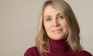Kobieta po 50-tce z niebieskimi oczami i blond włosami. Zastanawia się, jakie zabiegi na twarz dla 50 latki będą najlepsze.
