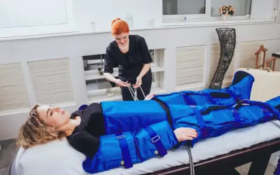 Kobieta w salonie piękności przechodzi zabieg drenażu limfatycznego. Widoczne są efekty zabiegu w postaci specjalnego kombinezonu uciskowego.