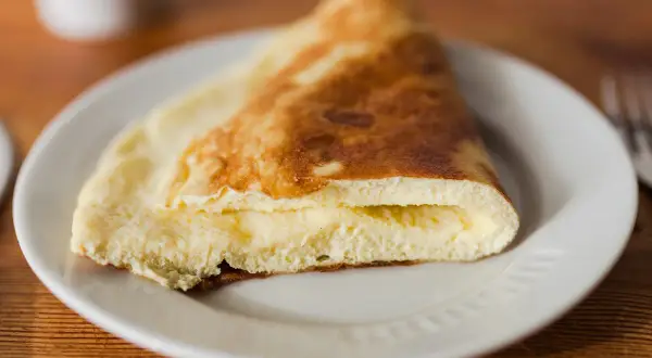 Puszysty omlet na parze, złożony na pół, z kremowym wnętrzem, podany na białym talerzu.
