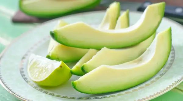 Plasterki awokado i ćwiartka limonki na talerzu. Zdrowe tłuszcze i niskie avocado kalorie.