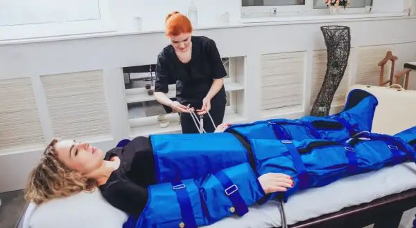 Kobieta w salonie piękności przechodzi zabieg drenażu limfatycznego. Widoczne są efekty zabiegu w postaci specjalnego kombinezonu uciskowego.