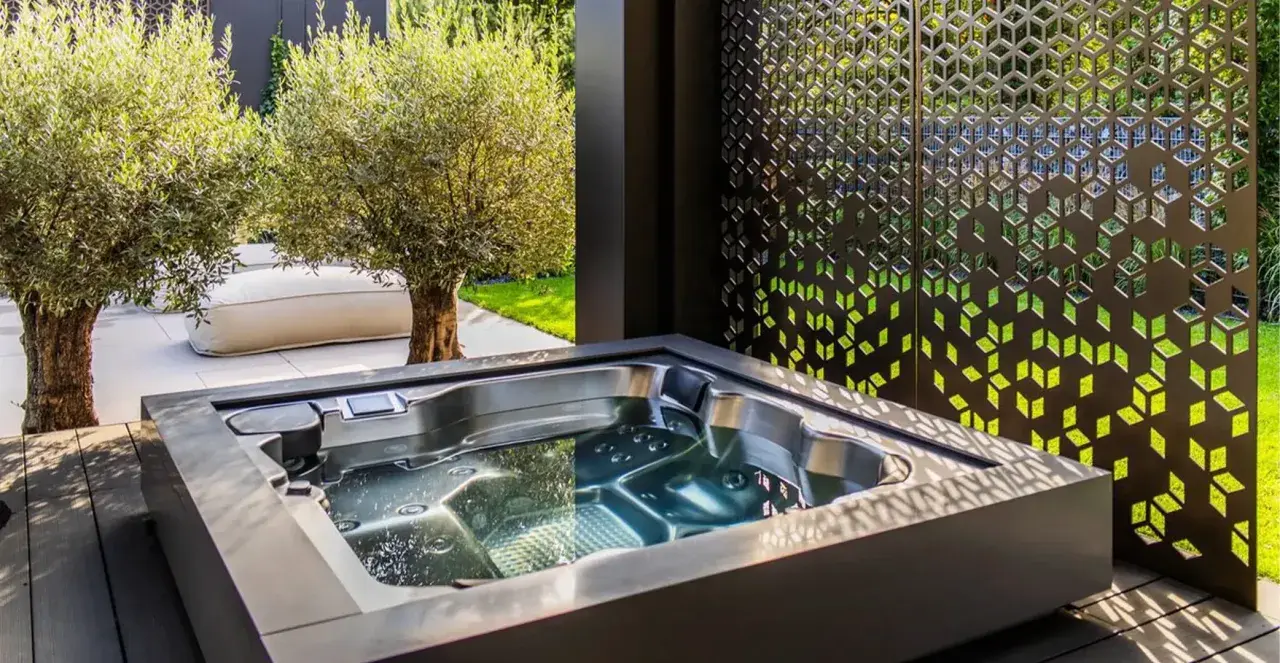 Nowoczesna strefa wellness z jacuzzi, otoczona oliwnymi drzewkami i ozdobnym panelem. Idealne miejsce na relaks.