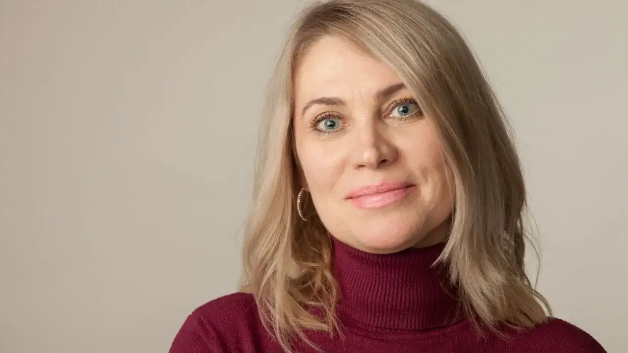 Kobieta po 50-tce z niebieskimi oczami i blond włosami. Zastanawia się, jakie zabiegi na twarz dla 50 latki będą najlepsze.