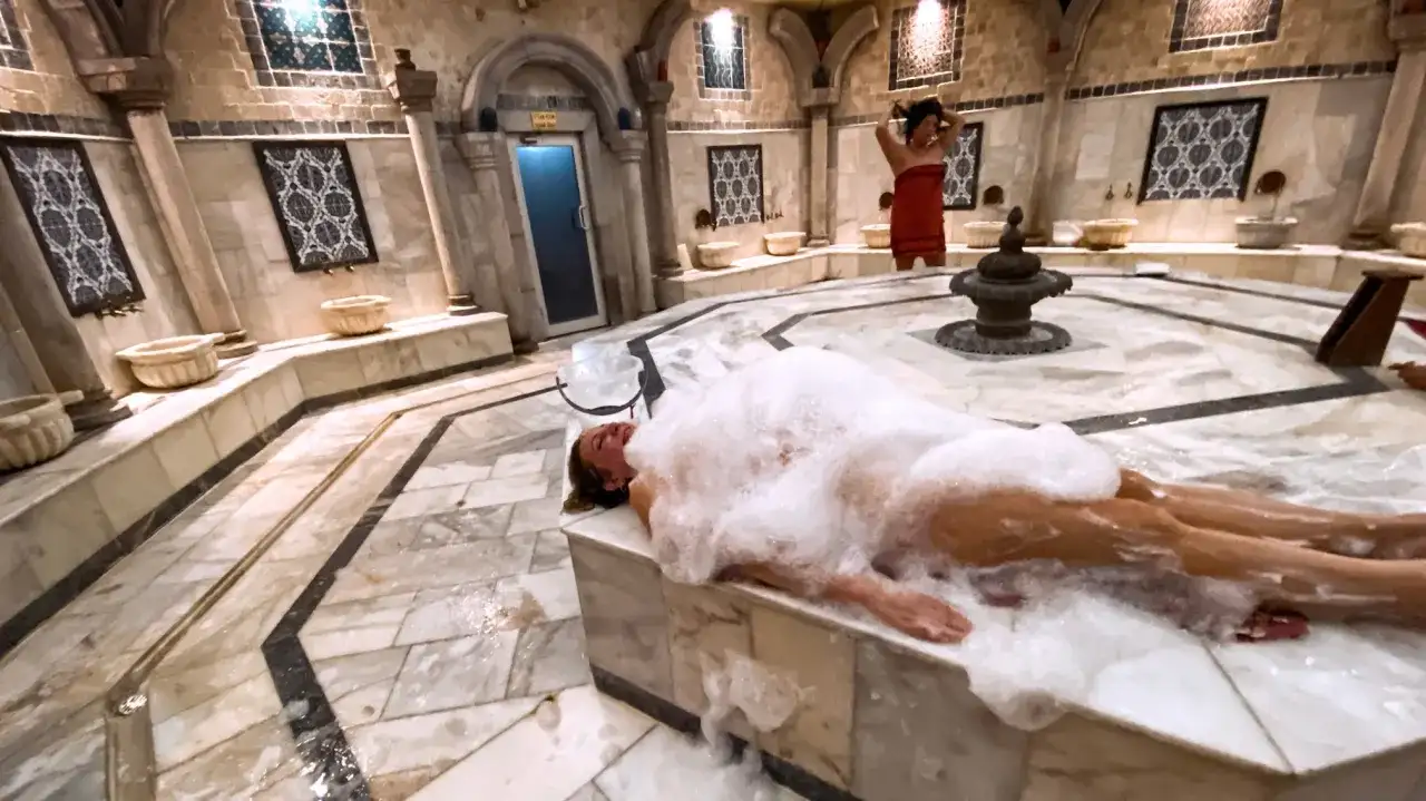 Relaks w pianie w tradycyjnym hammamie. Kobieta leży na marmurowym podwyższeniu, otoczona obfitą pianą.