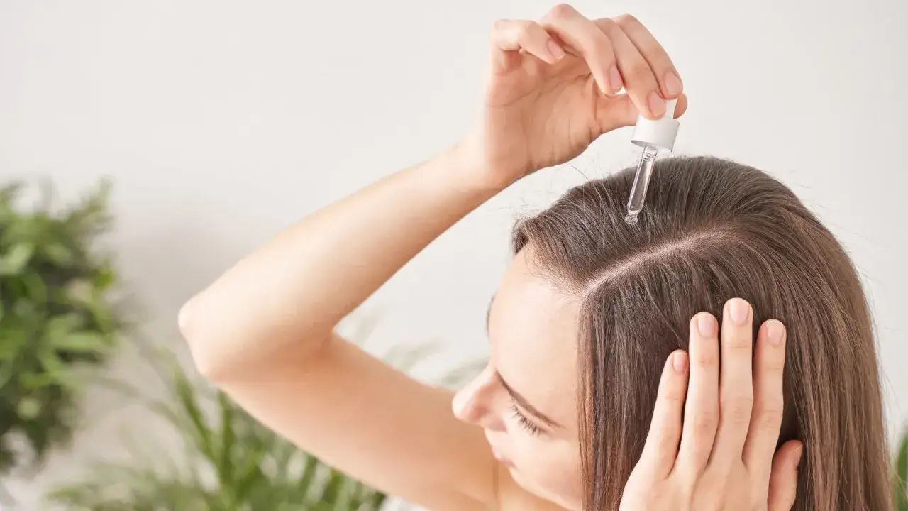 Kobieta aplikuje serum na skórę głowy, by zwalczyć alopecję.