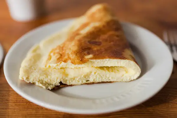 Puszysty omlet na parze, złożony na pół, z kremowym wnętrzem, podany na białym talerzu.