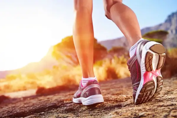 Nogi w butach sportowych stawiają kolejne kroki na kamienistej ścieżce. Słońce zachodzi za górami, tworząc ciepłą, złotą poświatę. Ile to 10000 kroków?