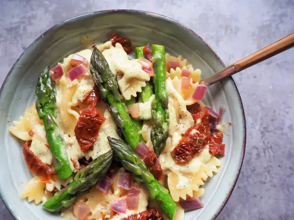 Makaron farfalle z zielonymi szparagami, suszonymi pomidorami i czerwoną cebulą w kremowym sosie.