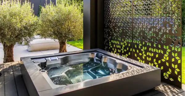 Nowoczesna strefa wellness z jacuzzi, otoczona oliwnymi drzewkami i ozdobnym panelem. Idealne miejsce na relaks.